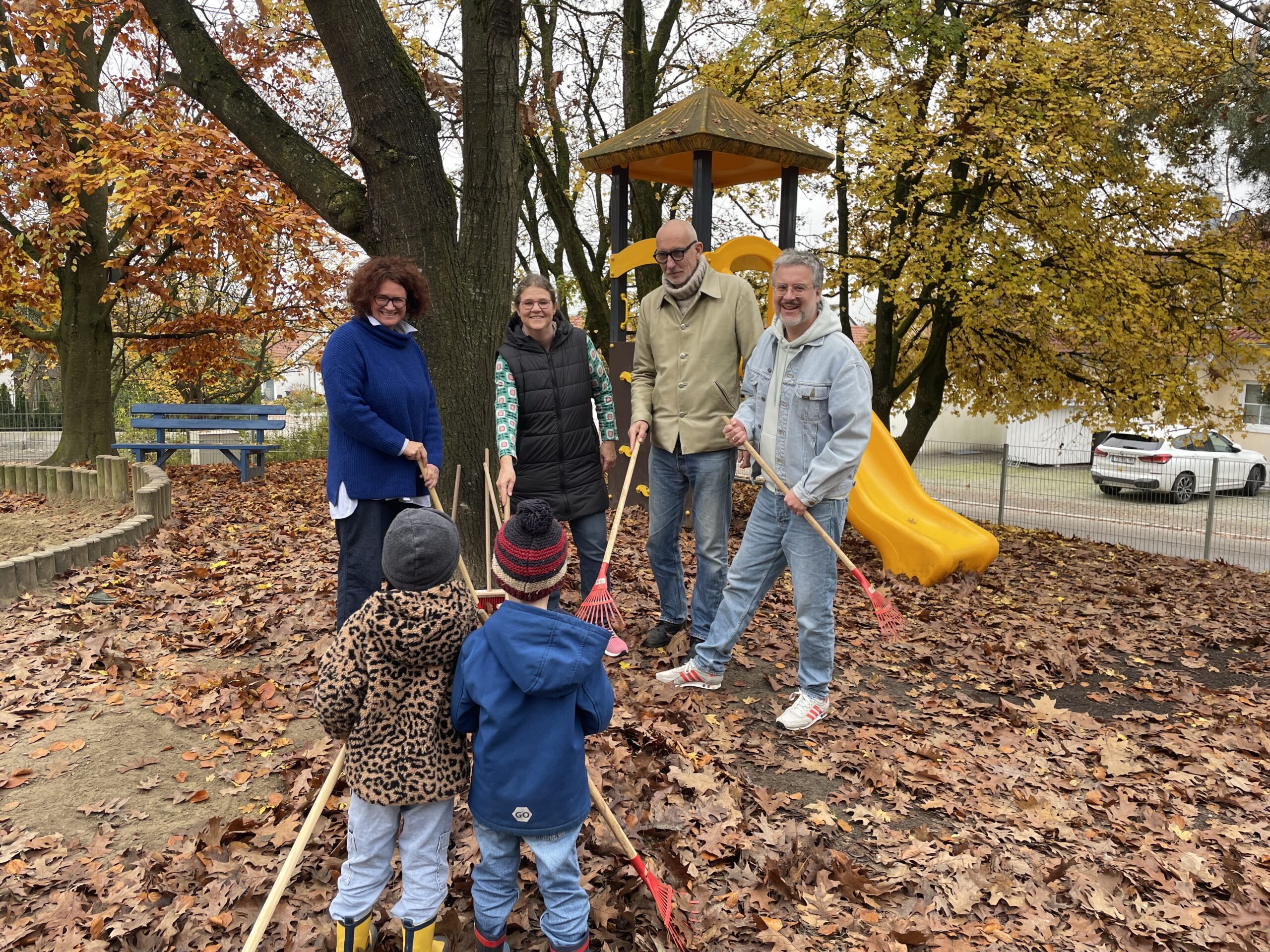 Gruppenfoto im herbstlichen Außenbereich des Kindergartens. v.l.n.r.: Marion Zott, Johanna Tiedeken (Kita-Leitung), Michael Zott und Josef Stadlmaier; vor den vier Erwachsenen stehen zwei Kinder mit dem Rücken zur Kamera. Alle halten kindgerechte Gartenwerkzeuge.
